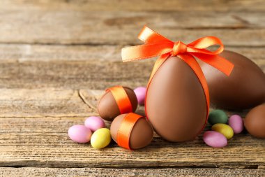 Mutlu Paskalyalar. Ahşap masada renkli şekerlemeli lezzetli çikolata yumurtaları, yakın plan. Metin için boşluk
