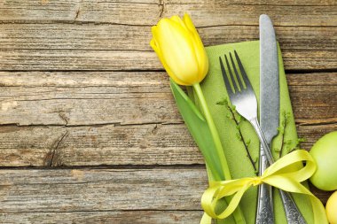 Easter table setting. Beautiful silverware with tulip and painted eggs on wooden background, top view. Space for text
