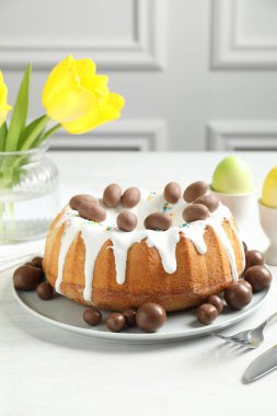 Lezzetli paskalya pastası, çikolatalı şekerler, boyanmış yumurtalar ve kapalı masa üzerinde sarı laleler, yakın plan.