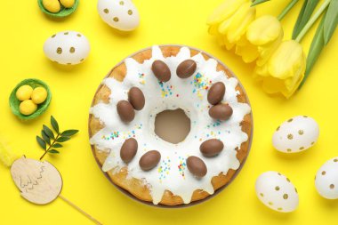 Lezzetli Paskalya pastası, boyanmış yumurtalar, lale çiçekleri ve sarı arka planda yeşil yapraklar.