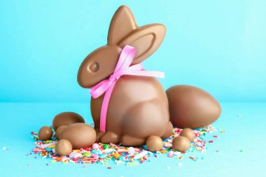 Çikolatalı Paskalya tavşanı, yumurtalar, şekerler ve açık mavi arka planda serpiştirmeler.
