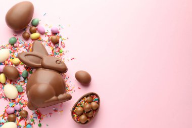 Çikolatalı Paskalya tavşanı, yumurtalar, şekerler ve pembe arka plana serpiştirilmiş şekerler, düz yatak. Metin için boşluk