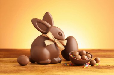 Çikolatalı Paskalya tavşanı, şekerli yumurtalar ve ahşap masaya serpiştirilmiş bej renkli arka plan.
