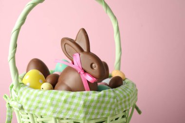 Çikolatalı Paskalya tavşanı ve hasır sepette pembe arka planda yumurtalar, yakın plan.