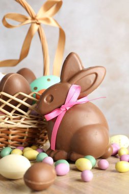 Çikolatalı Paskalya tavşanı ve hasır sepetteki yumurtalar ahşap masada açık gri arka planda, yakın plan