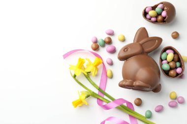Çikolatalı Paskalya tavşanı, çiçekler, beyaz arka planda kurdele ve yumurtalar, düz yatak. Metin için boşluk