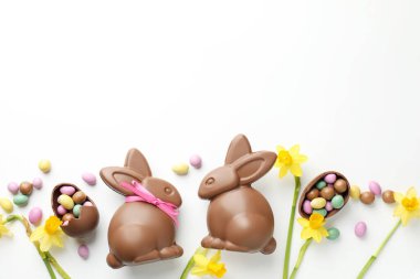 Beyaz arka planda çikolatalı Paskalya tavşanları, çiçekler, kurdele ve yumurtalar, düz yatak. Metin için boşluk