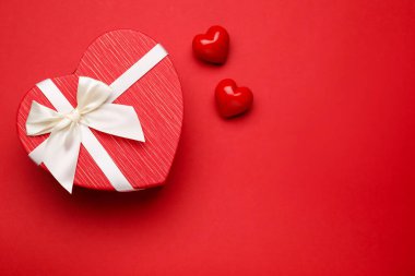 Sevgililer Günü. Güzel kalp şeklinde bir hediye ve kırmızı arka planda dekoratif kalpler. Metin için boşluk