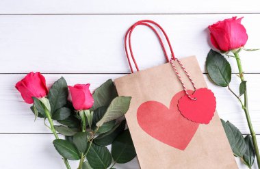 Beyaz ahşap arka planda güller olan hediye çantası, düz yatış. Sevgililer Günü