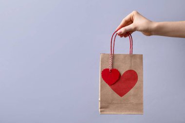 Arka planda kalbi açık, yakın plan ve mesaj için yeri olan hediye paketi taşıyan bir kadın. Sevgililer Günü