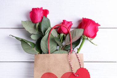 Beyaz ahşap arka planda güller olan hediye çantası, üst manzara. Sevgililer Günü
