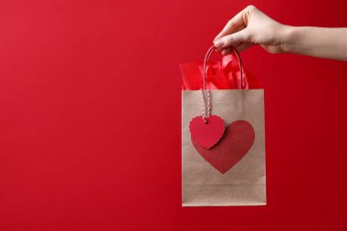 Kırmızı arka planda kalbi olan bir hediye çantası taşıyan kadın, yakın plan ve mesaj için yer. Sevgililer Günü