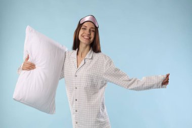 Maske takan güzel bir kadın ve açık mavi arka planda yastıklı şık pijamalar.