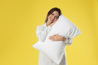 Sarı arka planda yastıklı şık pijamalı güzel bir kadın.