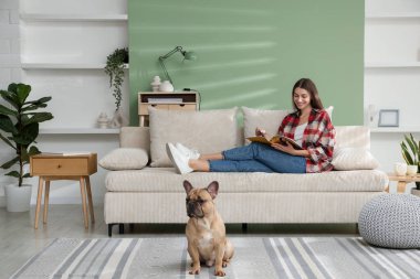 Dergisi olan bir kadın evdeki sevimli köpeğinin yanındaki kanepede dinleniyor.