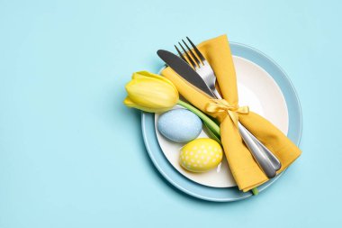 Paskalya kutlaması. Lale çiçekleri ve açık mavi arka planda boyanmış yumurtalarla süslü masa ayarı, üst manzara. Metin için boşluk