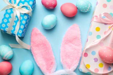 Mutlu Paskalyalar. Şirin tavşan kulakları, hediye kutuları ve açık mavi arka planda boyanmış yumurtalar, düz yatış.