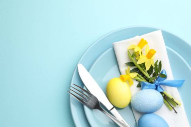 Paskalya kutlaması. Nergis çiçekleri ve açık mavi arka planda boyanmış yumurtalarla süslü masa ayarı, üst manzara. Metin için boşluk
