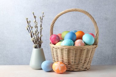 Hasır sepete boyanmış Paskalya yumurtaları ve bej masa üzerinde söğüt dalları.