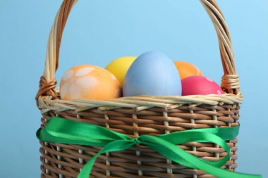 Hasır sepette boyalı Paskalya yumurtaları açık mavi arkaplan, yakın plan.