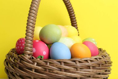 Hasır sepete boyanmış Paskalya yumurtaları. Sarı arka plana karşı, yakın plan.