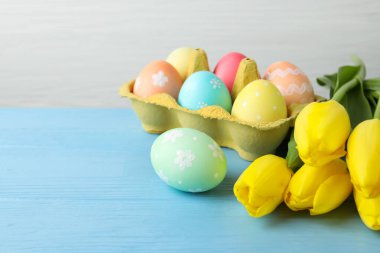 Kutuya boyanmış Paskalya yumurtaları ve açık mavi ahşap masa üzerinde güzel laleler. Yakın plan. Metin için boşluk