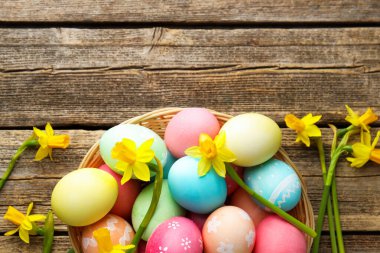 Hasır sepete boyanmış Paskalya yumurtaları ve ahşap masaya serilmiş güzel nergisler. Metin için boşluk