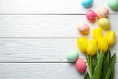 Boyanmış Paskalya yumurtaları ve beyaz ahşap masa üzerinde güzel laleler. Metin için boşluk