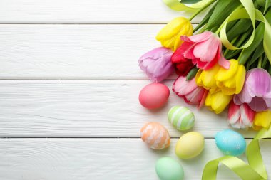 Boyalı Paskalya yumurtaları, güzel laleler ve beyaz ahşap masa şeritleri, düz bir döşeme. Metin için boşluk