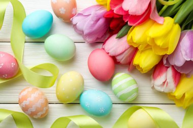 Painted Easter eggs, beautiful tulips and ribbons on white wooden table, flat lay
