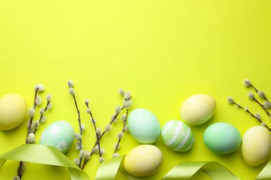 Painted Easter eggs, willow branches and ribbon on light green background, flat lay. Space for text