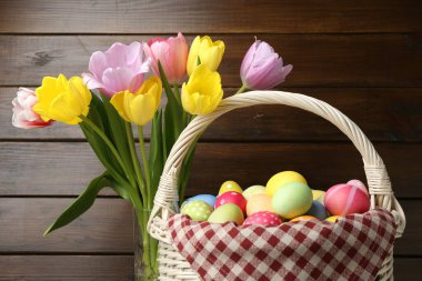 Hasır sepete boyanmış Paskalya yumurtaları ve ahşap arka planda güzel laleler. Yakın plan.