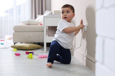 Evde çocuk güvenliği. Küçük çocuk içerideki elektrik prizinin fişini çekiyor.