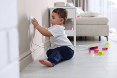 Evde çocuk güvenliği. Küçük çocuk içerideki elektrik prizinin fişini çekiyor.