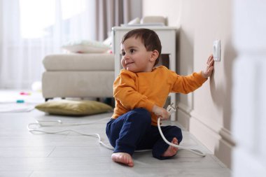 Evde çocuk güvenliği. Küçük çocuk içerideki elektrik prizinin fişini çekiyor.