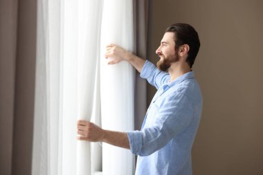 Evde şık pencere perdeleri açan adam