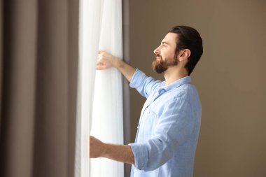 Evde şık pencere perdeleri açan adam