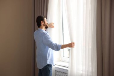 Evde şık pencere perdeleri açan adam