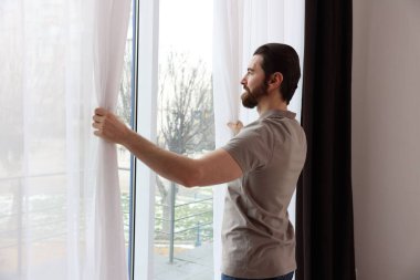 Evde şık pencere perdeleri açan adam