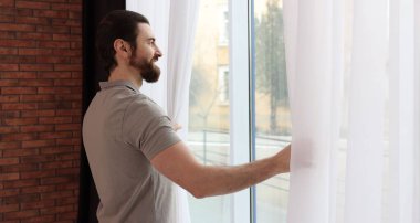 Evde şık pencere perdeleri açan adam