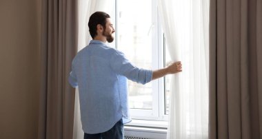 Evde şık pencere perdeleri açan adam