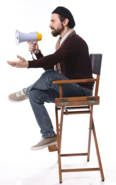 Kızgın film yönetmeni, beyaz arka planda sandalyede megafona bağırıyor.