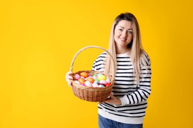Paskalya kutlaması. Sarı arka planda boyanmış yumurta dolu sepeti olan gülümseyen kadın, mesaj için yer.