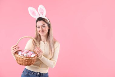 Paskalya kutlaması. Saç bandı takmış, tavşan kulaklı, pembe arka planda içi yumurta dolu sepetli gülümseyen bir kadın. Mesaj için yer var.