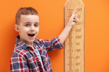 Küçük çocuk turuncu duvarın yanında boyunu ölçüyor.