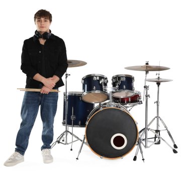 Kulaklıkları, bagetleri ve davulları beyaz arka planda olan genç bir çocuk.