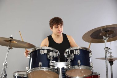 Çubuklu genç çocuk gri arka planda davul çalmayı öğreniyor.