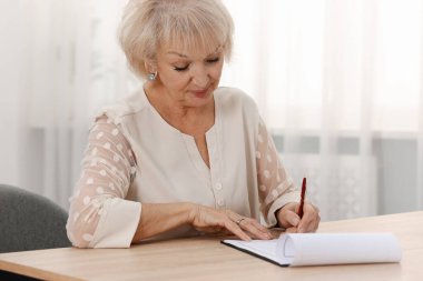 Ahşap masada son dilek ve vasiyetnameyi imzalayan üst düzey bir kadın.