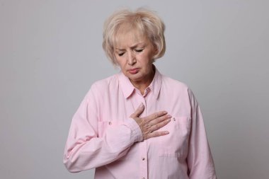 Kalp krizi geçirdi. Gri arka planda göğüs ağrısı çeken yaşlı bir kadın.