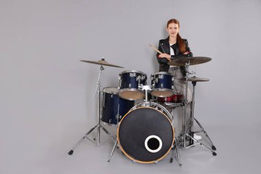 Açık gri arka planda bagetleri ve davulları olan genç bir kız.